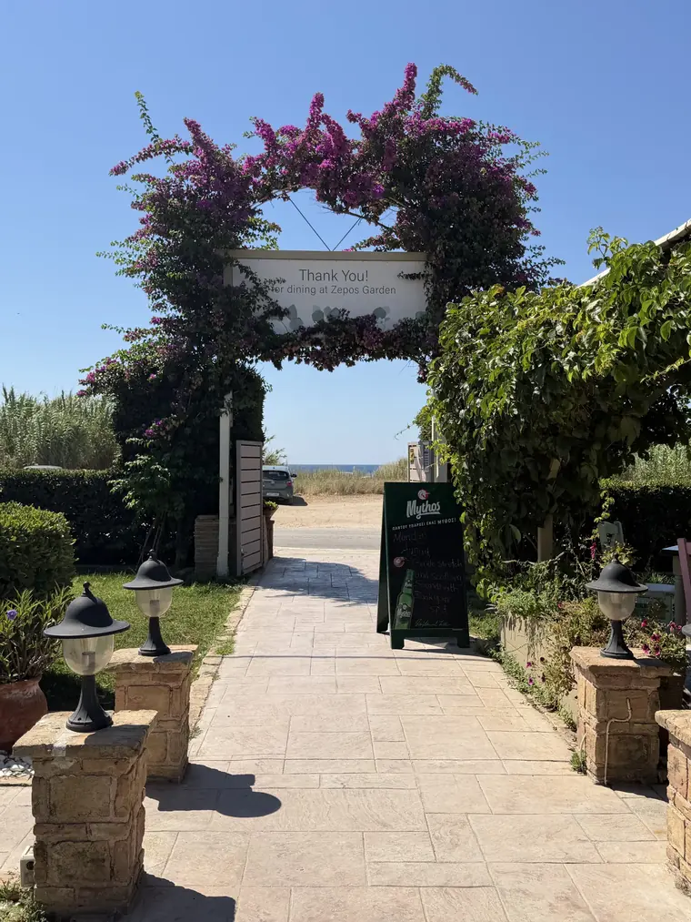 The bougainvillea arch at the entrance, its sign still thanking you for dining at Zepos Garden, with the sea beyond